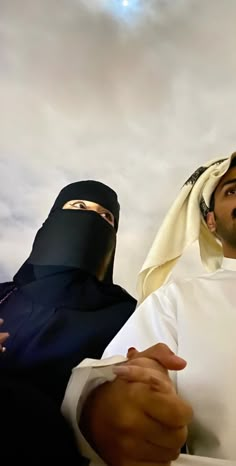 two men dressed in burkas standing next to each other under a cloudy sky