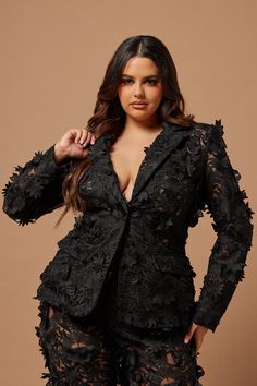 a woman is posing for the camera wearing a black suit with lace detailing and an open lapel collar