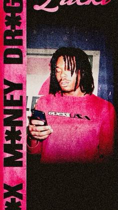 a man with dreadlocks is looking at his cell phone while wearing a pink shirt