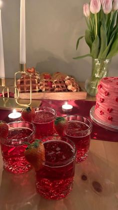 several glasses filled with liquid sitting on top of a table next to a cake and candles