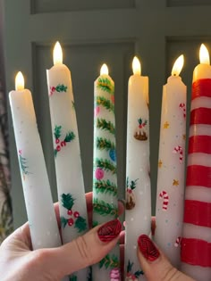 a person holding five candles in front of each other with christmas decorations on them,