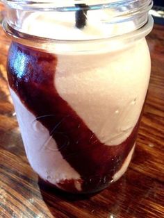 a glass jar filled with ice cream on top of a wooden table next to a spoon