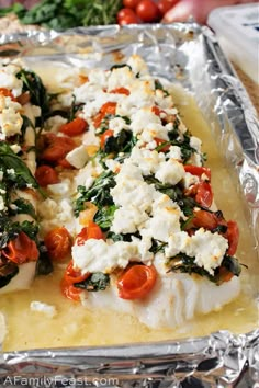 baked fish with tomatoes, spinach and feta cheese on aluminum foil lined baking sheet