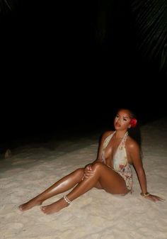 a woman sitting on top of a sandy beach next to a palm tree at night