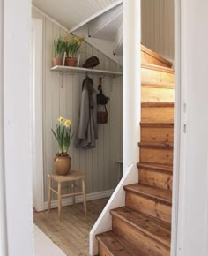 there is a coat rack on the wall next to some stairs and a table with flowers in it