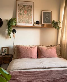 there is a bed with pink sheets and pillows in the room that has plants on the wall above it