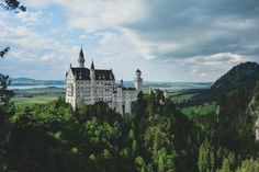 a large castle sitting on top of a lush green hillside next to a forest filled with trees