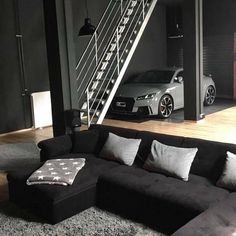 a living room with a black couch and stairs in front of a car on the floor