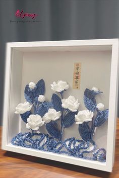 three white flowers in a shadow box on top of a wooden table with chinese writing