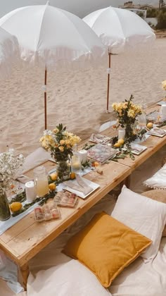 an outdoor dining table set up on the beach with white umbrellas and yellow flowers