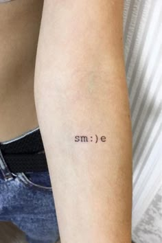 a woman's arm with the word smile tattooed on her left arm, in black ink