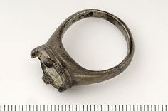 an old silver ring with a face on it and a ruler in the foreground