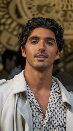 a close up of a person wearing a white jacket and black shirt with a coat over his shoulders