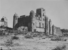 black and white photograph of an old castle in the middle of dirt field with trees