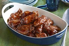 a blue casserole dish filled with meat and sauce on a green table cloth