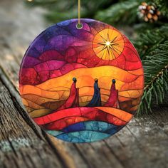 a colorful ornament hanging from a christmas tree on a wooden table with pine branches