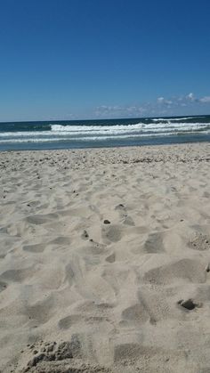 a surfboard sitting on top of a sandy beach next to the ocean with waves coming in