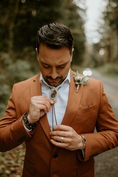 a man in an orange suit adjusts his flower on his tie while standing next to the road