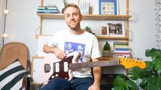 a man sitting in a chair holding an electric guitar and looking at the camera while he is playing it