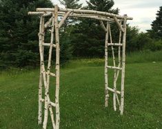 two wooden archways made out of branches in the grass with trees in the background