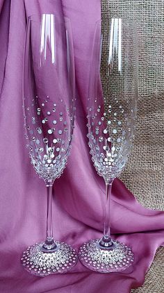 two wine glasses sitting next to each other on a purple cloth