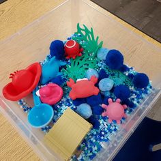 a plastic container filled with different types of sea animals and sand on top of a wooden table