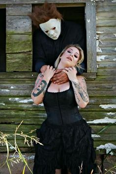 a woman in black dress standing next to a man wearing a mask