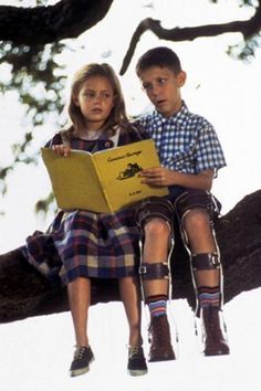 two children are sitting on a tree branch and reading a book in front of them