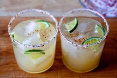 two glasses filled with drinks sitting on top of a wooden table