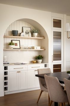 a dining room table and chairs in front of a wall shelf with shelves on it