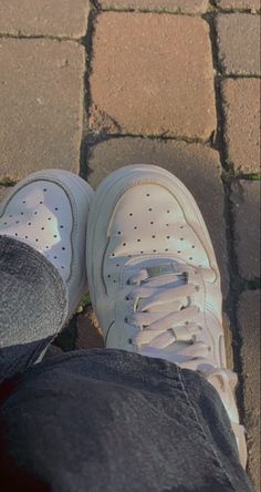 a person wearing white tennis shoes standing on brick walkway with their feet in the air