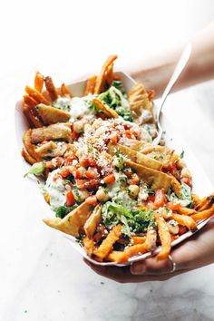 a person is holding a tray full of fries and salad with dressing on top, ready to be eaten