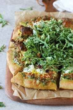 a pizza topped with greens on top of a wooden cutting board next to a napkin