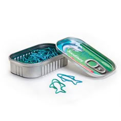 an open tin with fish hooks in it on a white surface next to some paper clips