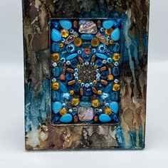 a blue and brown square shaped object with many different colored beads on it's surface