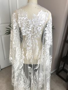 a white wedding dress with sheer sleeves and flowers on the front, sitting on a mannequin