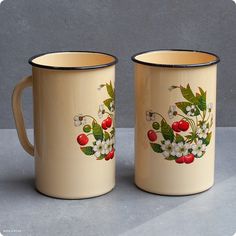 two coffee mugs decorated with cherries and white flowers are sitting next to each other