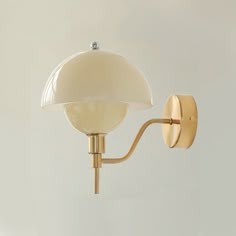 a wall light with a white shade on it's side and a gold arm