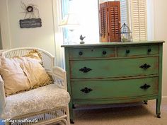 a green dresser sitting next to a white chair in a room with shuttered windows