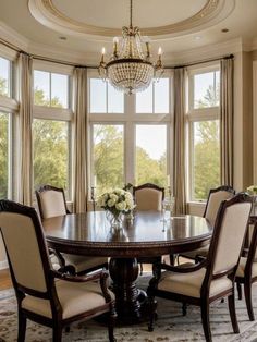 a dining room table with chairs and chandelier in front of two large windows