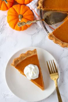 a slice of pumpkin pie on a white plate with whipped cream and gold fork next to it