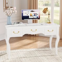 a white desk with a computer on it and flowers in a vase next to it