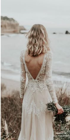 the back of a woman's wedding dress as she walks along the beach with her bouquet in hand