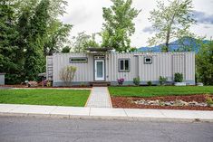 a house made out of shipping containers sitting on the side of a road in front of some trees