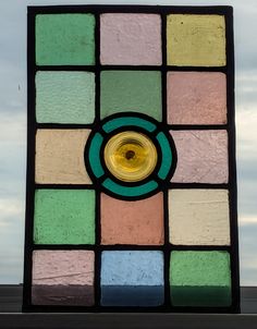 a multicolored glass window with a yellow light in the center and blue sky behind it