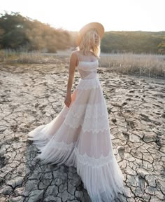 a woman in a white dress and hat standing on dry land with her back to the camera