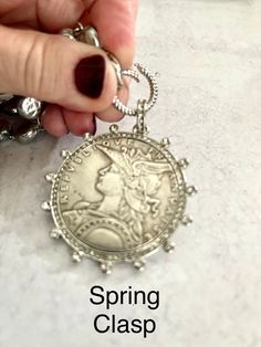 a person is holding onto a silver necklace with a coin on it and the words spring class written below