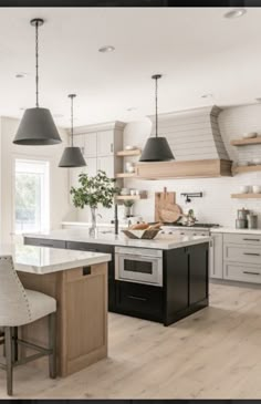 a kitchen with an island and two pendant lights hanging over the stove top, along with chairs