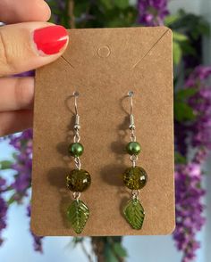 a pair of earrings with green beads and leaves hanging from the ear hooks on a card