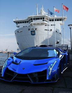 a blue sports car parked in front of a cruise ship with flags flying above it